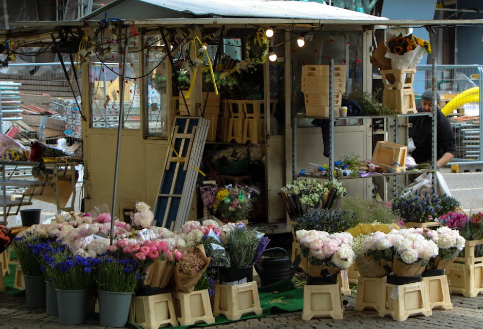 A flower stall at Brockley Market featuring an assortment of fresh flowers arranged in buckets and wrapped bouquets. The display includes pink, white, and purple blooms, such as peonies, roses, and la