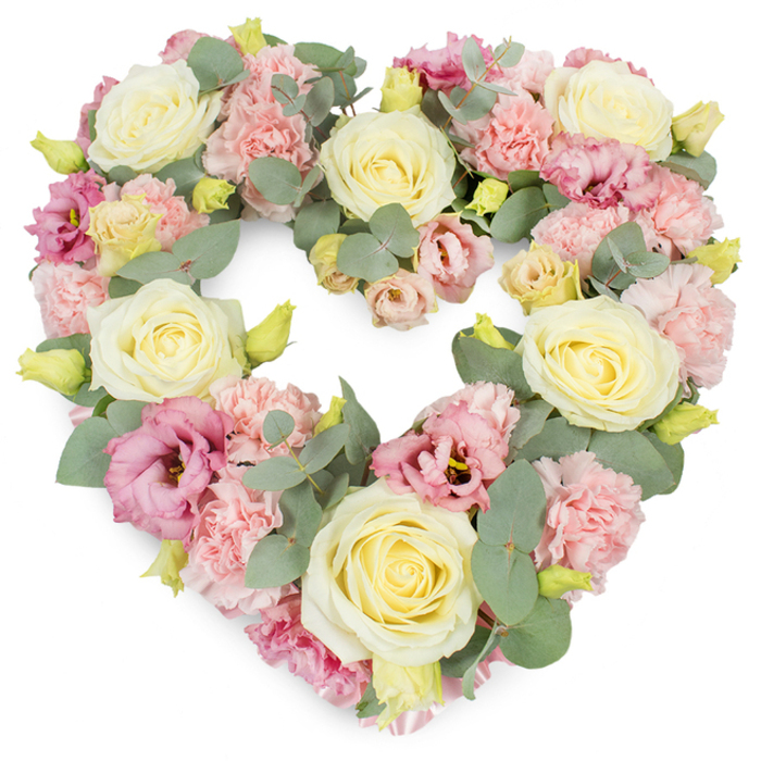 A luxurious heart-shaped funeral tribute sits against a clean white background, its pastel flowers arranged so closely that the entire form looks like a cushion of petals. The heart is built around several prominent cream and soft yellow roses, each one fully open, with velvety petals swirling outward from tight centres into generous, cup-shaped blooms that immediately draw the eye. Between and around these anchor roses, delicate light pink carnations provide a beautifully ruffled texture, their edges slightly curled and feathered, creating gentle shadows that give the design depth. Richer tones appear in the mauve and magenta-pink lisianthus blooms, whose softer, more open petals unfurl in relaxed, trumpet-like shapes, bringing a graceful contrast to the more classic structure of the roses and carnations. Throughout the arrangement, stems of silvery-green eucalyptus weave in and out, their round to oval leaves cooling the palette and adding a gentle, aromatic greenery reminiscent of calm walks through Brockley and nearby Telegraph Hill. Small, tightly closed yellow-green buds are tucked between the larger blooms, hinting at new growth and symbolising hope alongside remembrance. Every flower is placed tightly together to create a dense, complete heart, its edges clearly defined and its centre filled, giving the impression of abundance and care. The overall mood is tender, peaceful, and respectful, ideal for local funerals, cremation services, or memorial gatherings in Brockley. It feels like a heartfelt message made visible in petals and leaves, a lasting symbol of love and sympathy for families wishing to honour someone special with a soft, pastel tribute.