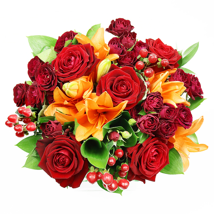 From a top-down viewpoint against a spotless white background, this richly hued bouquet is an exercise in layered warmth and floral craftsmanship. Prominent deep-red roses, plump and fully bloomed, anchor the design with their velvety textures and softly cupped petals that suggest intimacy and long-standing affection. Interlaced among them are vivid orange Asiatic lilies whose trumpet-shaped petals and exposed stamens add architectural drama and a lively, uplifting note; some of these lilies sit wide open while others are caught mid-unfurl, promising continued bloom. Tight clusters of wine-hued spray roses supply concentrated colour and a sumptuous, almost textile-like density that deepens the composition. Here and there, small clusters of glossy hypericum berries introduce bright pinpoint highlights and a firmer, round texture that contrasts with the petals' soft give. Lush green foliage, likely ruscus or salal, peeks through the flowers, its broad leaves providing a cool counterpoint and helping to shape the bouquet's rounded silhouette. The soft, even studio lighting renders colour saturation true and rich, making the reds and oranges glow without losing subtle detail. Imagining this arrangement in a Brockley flat overlooking Hilly Fields or as a surprise left at a doorstep on St John's Vale, the bouquet reads as both celebratory and tender-an ideal choice for anniversaries, heartfelt thank-yous, or autumnal home decor. It's the kind of thoughtfully balanced design a local florist would suggest for someone seeking warmth and classic romance with modern flair.