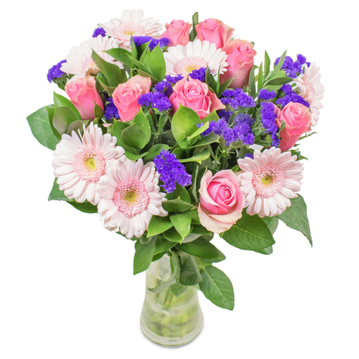 A radiant floral arrangement stands gracefully in a clear glass vase, set against a crisp backdrop that highlights every intricate detail. Approximately seven to nine tender pink roses, many still partially closed with their classic spiral forms, form the core of the bouquet, symbolising affection and timeless beauty. Nestled among them are five to seven pale pink gerbera daisies, each bloom defined by its broad, cheerful head and finely ruffled petals fading gently toward creamy white centers. The artistry shines in the seamless harmony of colour and form, as vivid purple statice clusters spring from the ensemble-these bold fillers add dimension, texture, and a spirited contrast that evokes the artistic flair of Brockley's local galleries. Lush, robust greenery fills out the base, the deep green leaves reminiscent of Brockley's tranquil gardens, adding not only visual fullness but providing a faint suggestion of earthy woodland fragrance. The polished glass vase, stems visible and submerged in cool, fresh water, completes the sophisticated presentation, suggesting the hand-gathered feel of locally sourced blooms in the heart of Brockley. This distinctive arrangement, perfect for occasions from anniversaries on Wickham Road to cheerful everyday adornment for a home off Geoffrey Road, carries a sense of vibrant celebration and heartfelt care, offering a gift of lasting freshness and refined beauty.